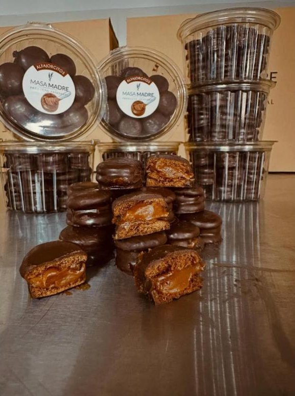 Alfajorcitos de chocolate apilados junto a sus potes transparentes